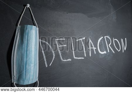 A Blue Medical Mask And Deltacron Written In Chalk On The Board. Deltacron Is A New Version Of Covid