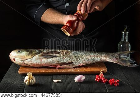 Professional Chef Prepares Silver Carp Herring In The Restaurant Kitchen. The Cook Sprinkles Pepper 