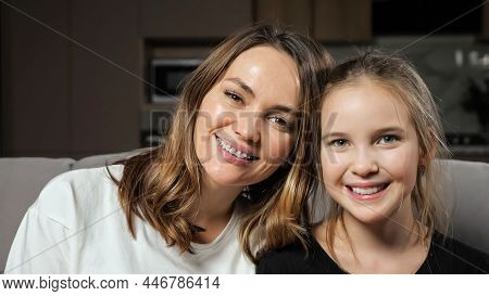 Satisfied Mother And Teen Daughter In White And Black T-shirts Smile Widely Looking In Camera Sittin