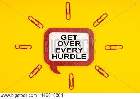 On A Yellow Background, Paper Clips And A Mental Plaque With The Inscription - Get Over Every Hurdle