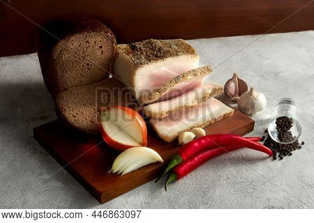 A Piece Of Ham With Bread On A Cutting Board. Next To The Onion, Garlic And Paprika.