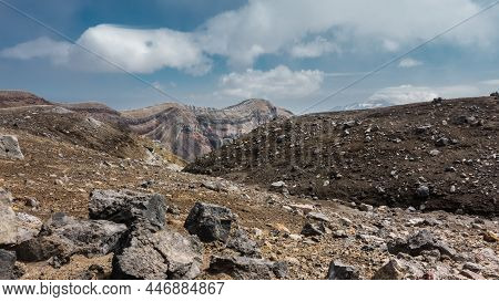 The Top Of An Active Volcano. Rocky Soil Is Visible, The Layered Structure Of The Crater. Blue Sky W