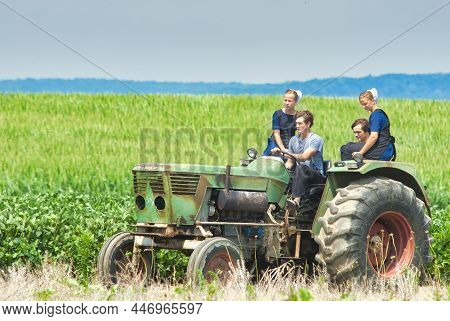 Ronks, Pennsylvania, July 2021 - Amish Boy And Girl Teenagers Riding On A Old Tractor Thru Farmlands