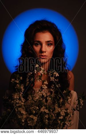 Portrait Of A Girl Who Looks Like A Nymph, In Neon Lighting With A Halo Over Her Head And Flowers In