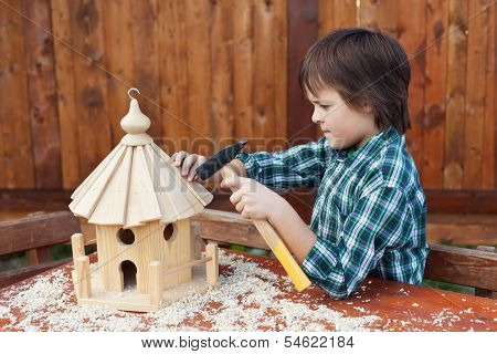 Boy building a bird house - mounting the last roof piece with a nail and hammer