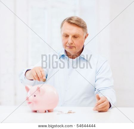savings, oldness,business and banking concept - old man putting coin into big piggy bank