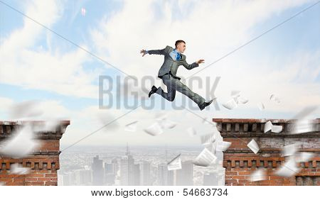 Young businessman jumping over bridge gap. Risking in business