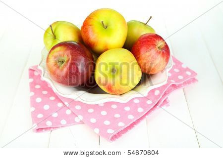 Juicy apples on plate on white wooden table