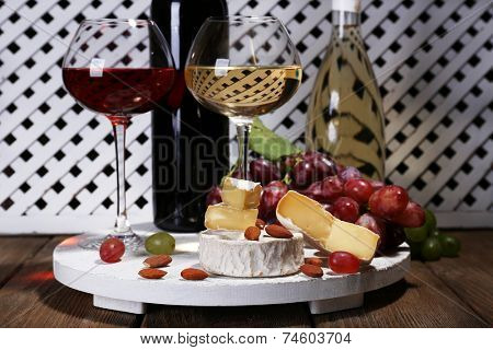 Supper consisting of Camembert cheese, wine and grapes on stand on wooden table on white fence background