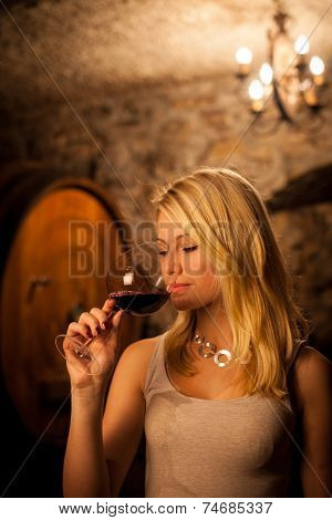 Beautiful Young Blond Woman Tasting Red Wine In A Wine Cellar