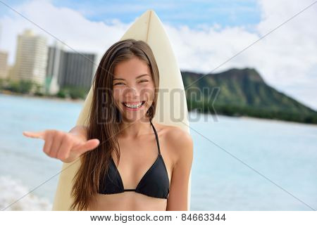 Surfer girl surfing showing mahalo shaka hand sign signal saying hello on Waikiki Beach, Oahu, Hawaii. Female bikini woman holding surfboard smiling happy on Hawaiian beach. Asian Caucasian model.