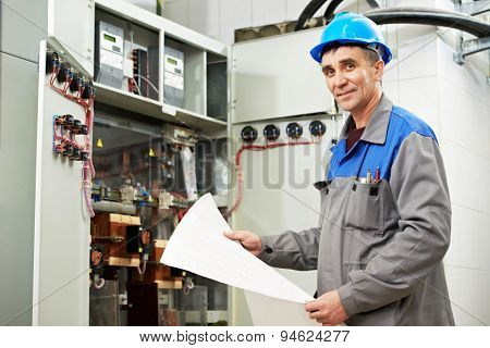 electrician builder engineer inspector with electrical scheme plan near the fuse box