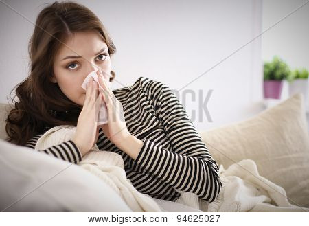 Portrait of a sick woman blowing her nose while sitting on the sofa