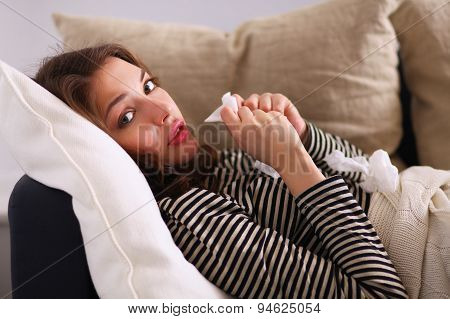 Portrait of a sick woman blowing her nose while sitting on the sofa