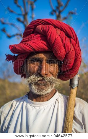 GODWAR REGION, INDIA - 13 FEBRUARY 2015: Rabari tribesman holds traditional axe and stands on field. Rabari or Rewari are an Indian community in the state of Gujarat.