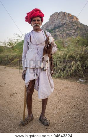 GODWAR REGION, INDIA - 13 FEBRUARY 2015: Elderly Rabari tribesman stands and holds goatling and traditional axe. Rabari or Rewari are an Indian community in the state of Gujarat.