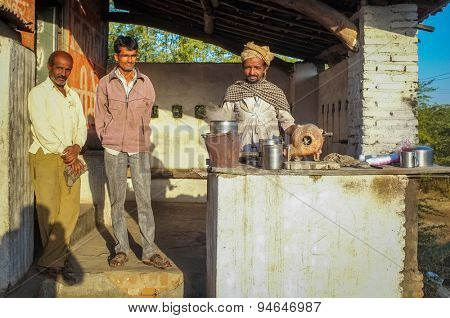 GODWAR REGION, INDIA - 14 FEBRUARY 2015: Man prepares milk tea with traditional wind turbine for making fire. Two customers wait for it to be finished.