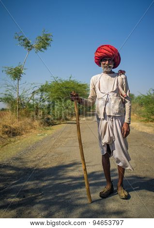 GODWAR REGION, INDIA - 14 FEBRUARY 2015: Elderly Rabari tribesman with big red turban and cane stands on road. Rabari or Rewari are an Indian community in the state of Gujarat.