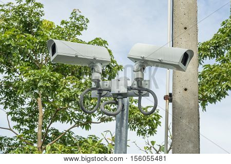 security CCTV cameras on a pole with the green tree background