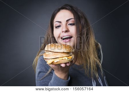 Happy beautiful young plus size model posing with hamburger on a gray studio background xxl woman eating burger fast food and unhealthy nutrition concept