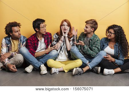 Surpsised redhead young woman sitting with her friends over yellow background