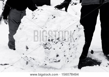 Black and white image of a child rolling a large snowball in the snow to make a snowman