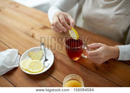 health, traditional medicine and ethnoscience concept - close up of woman adding lemon to tea cup