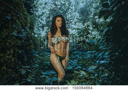 outdoors portrait of sensual young woman in underwear leaf looking at the camera in the forest