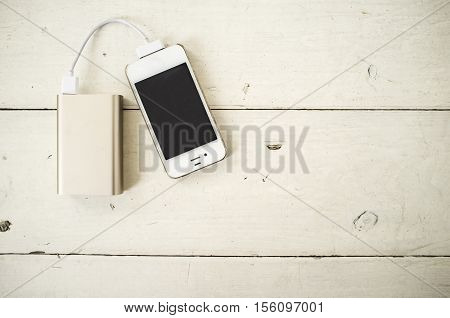 Smartphone is charged from the portable charging device for shabby the wooden table painted in white color
