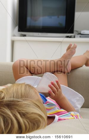 Dziecko pije mleko czekoladowe w butelce, leżące samotnie na kanapie i oglądać TV w pliku DVD