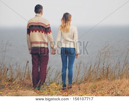 Young attractive couple in knitted sweaters standing on a cliff at sea shore and hugging