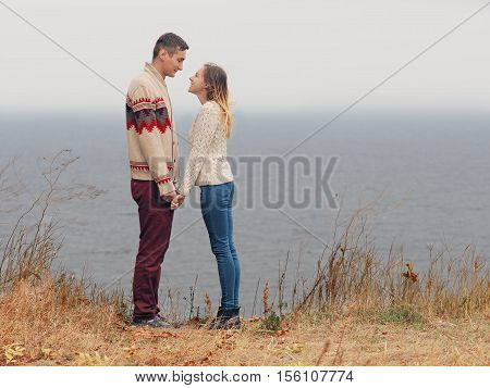 Young attractive couple in knitted sweaters standing on a cliff at sea shore and hugging