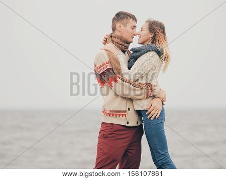 Young attractive couple in knitted sweaters on a cliff on sea shore hugging and holding hands creative toning