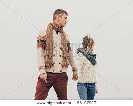 Young attractive couple in knitted sweaters on a cliff on sea shore hugging and holding hands creative toning