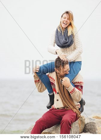 Young attractive couple in knitted sweaters having fun at sea shore man jokingly bites his girlfriend