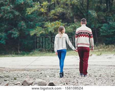 Young attractive couple in knitted sweaters on a cliff on sea shore hugging and holding hands creative toning