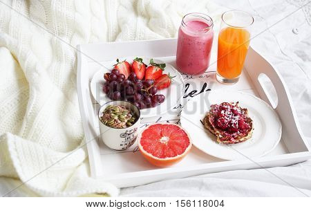 A delicious brakfast in bed with juice smoothie fruit granola and pancakes