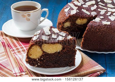 Baking in multicooker. Delicious homemade chocolate cake with curd-coconut balls on a blue wooden table. Decorated with coconut crunch. Served with tea