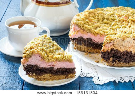 Baking in multicooker. Homemade festive multilayer cake with jam chocolate marshmallows streusel and a cup of tea on a blue wooden background. Selective focus