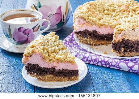 Baking in multicooker. Homemade festive multilayer cake with jam chocolate marshmallows streusel and a cup of tea on a blue wooden background. Selective focus