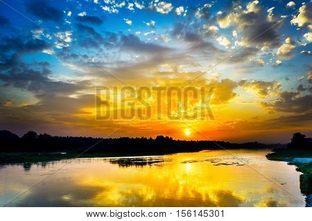 Beautiful lake landscape with vivid sunrise on the cloudy sky. River landscape. Beautiful summer landscape with golden sunset.