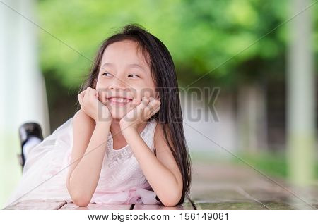 Portrait of a smiling little girl in pink dress looking sideways and lying on wooden table