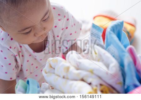 Baby with heap of colorful clothes in the room