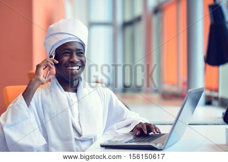 Sudanese business man in traditional outfit using mobile phone in office.