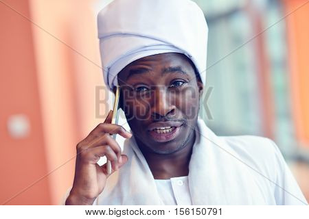 Sudanese business man in traditional outfit using mobile phone in office.