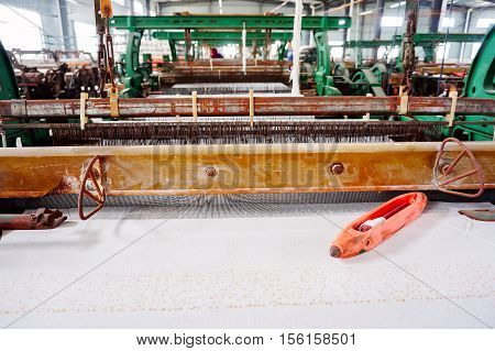 A row of textile looms weaving cotton yarn in a textile mill.