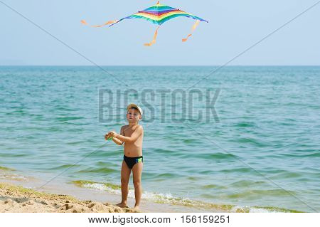 Little boy resting and playing on the beach with a kite