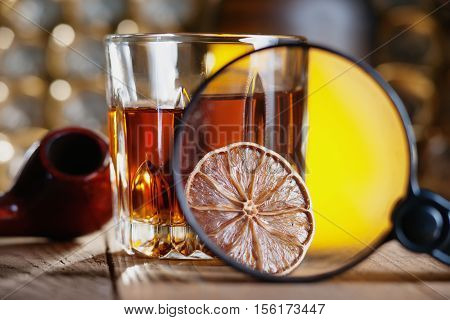 Glass of whiskey, magnifying glass, lemon and smooking pipe