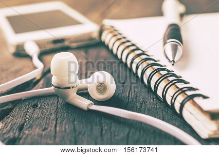 White Headphones, Smartphone With Notebook On Wood Table Background Vintage Color.