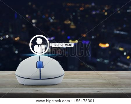 Wireless computer mouse with businessman and magnifying glass icon on wooden table over blur light city tower Recruitment concept